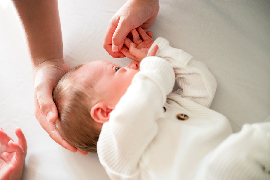 A newborn baby in a white sleeper rests in his crib during a session with a lifestyle newborn photographer in Houston TX. 