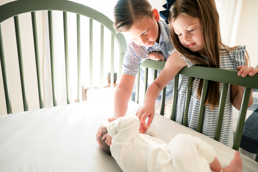 Older siblings watch over their newborn sibling in his crib during an in home newborn session in Houston TX. 