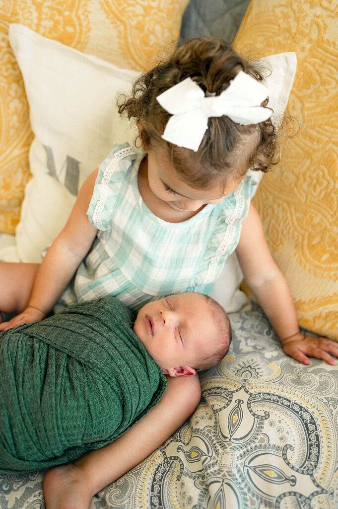 A toddler looks admiringly at her newborn brother during a Cypress TX newborn photoshoot 