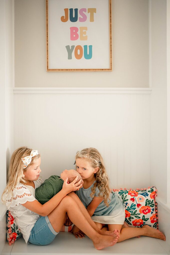 A photo taken during newborn photography in Houston depicts two young girls admiring their new brother 