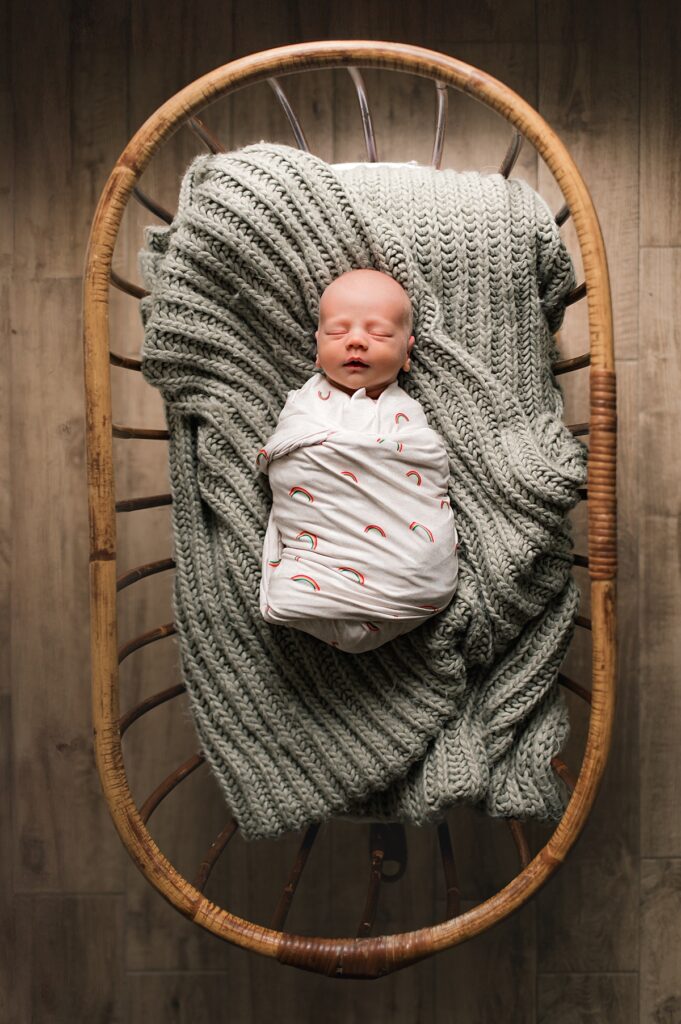 A swaddled Texas newborn is shown atop a sage colored knitted throw during a lifestyle in-home newborn session.