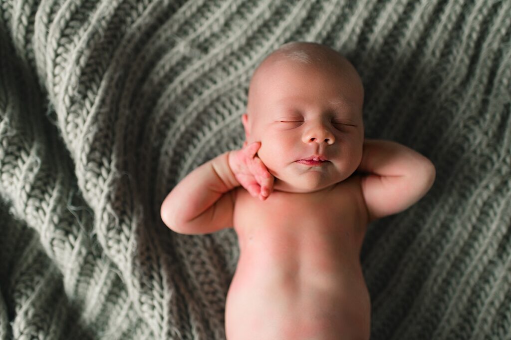 A sleeping newborn is shown atop a sage colored knitted throw during a lifestyle in-home newborn session with Texas newborn and family photographer, Mel B Photo.