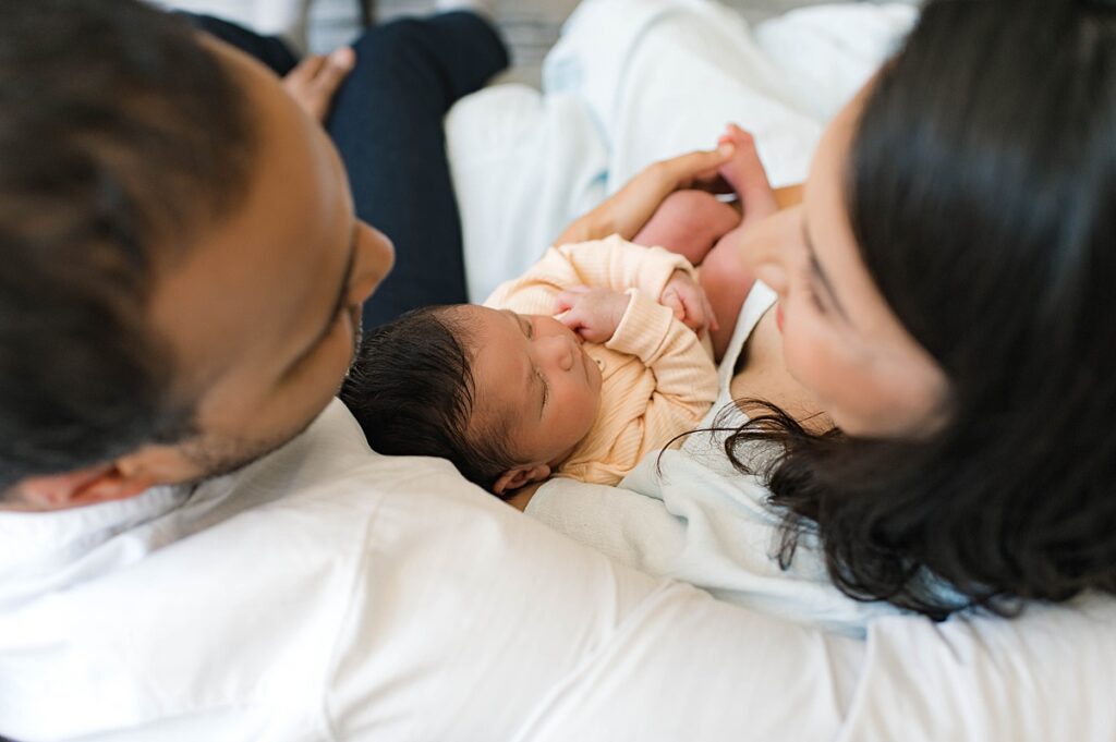 A Cypress, Texas couple are pictured from above cradling their newborn daughter wearing a soft yellow onesie during an in-home photo session with Towne Lake newborn photographer, Mel B Photo.