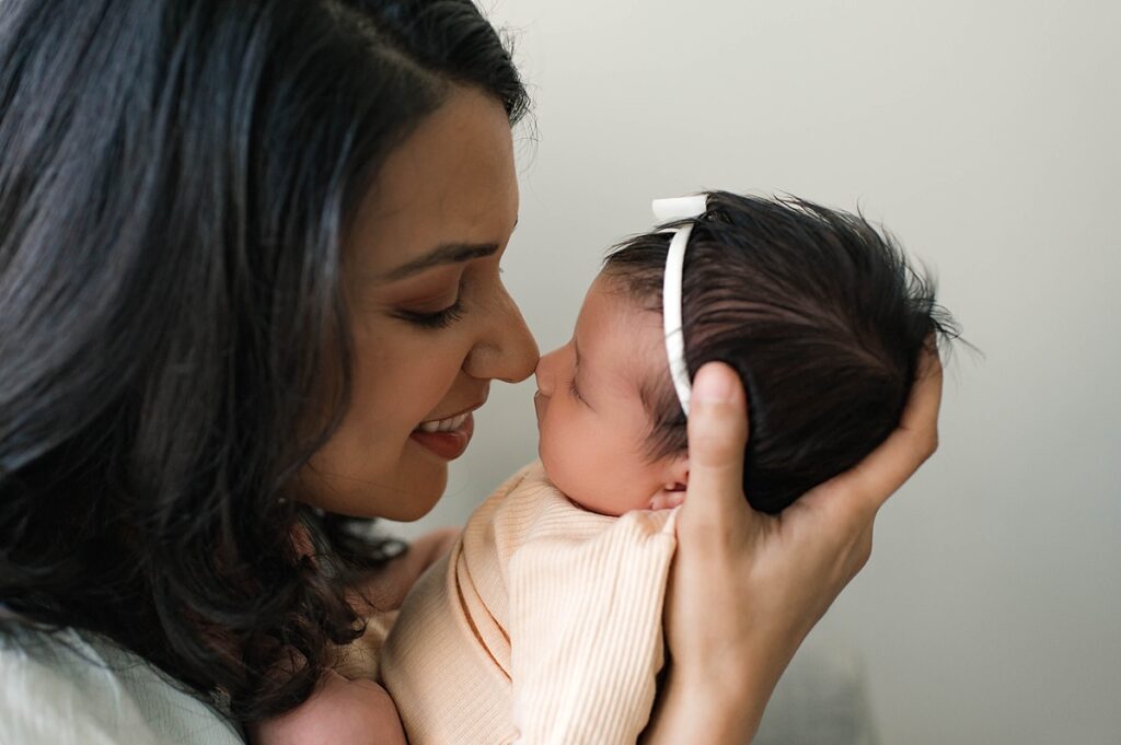 A new mother with dark hair touches her nose to her newborn daughter's face in her Cypress, TX in home newborn photoshoot.