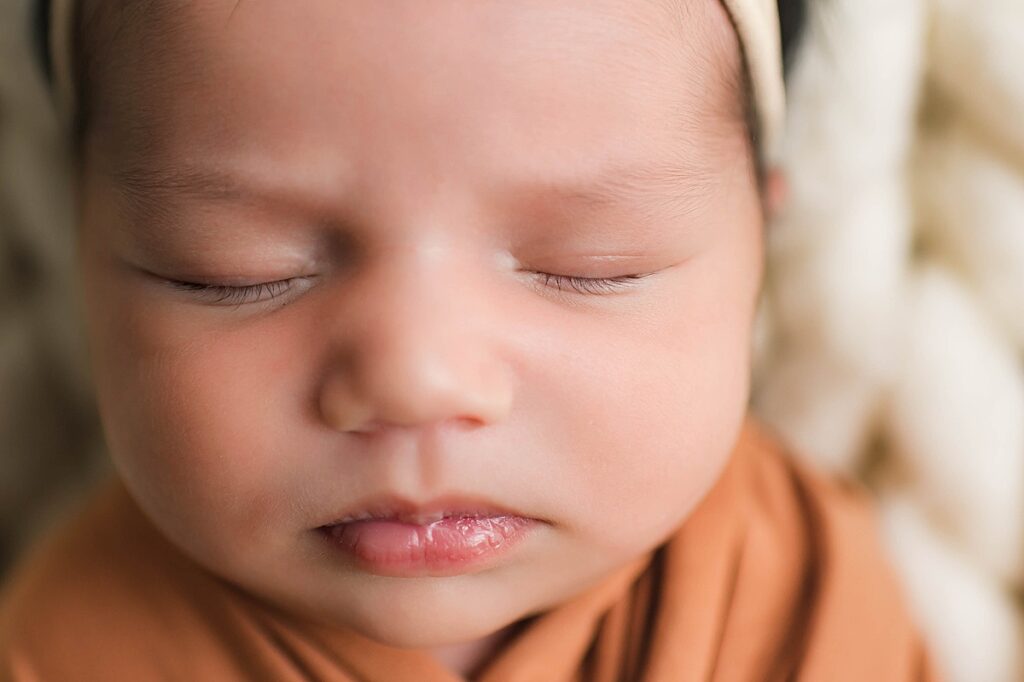 A Cypress, TX newborn is pictured in a burnt orange swaddle during an in-home newborn session with Towne Lake newborn photographer, Mel B Photo.