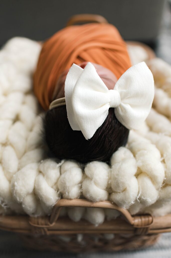 A Cypress, TX newborn is pictured in a burnt orange swaddle and white bow during an in-home newborn session with Towne Lake newborn photographer, Mel B Photo.