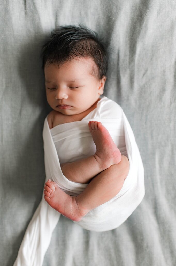 A Cypress, TX newborn with dark hair is pictured in a white swaddle during an in-home newborn session with Towne Lake newborn photographer, Mel B Photo.