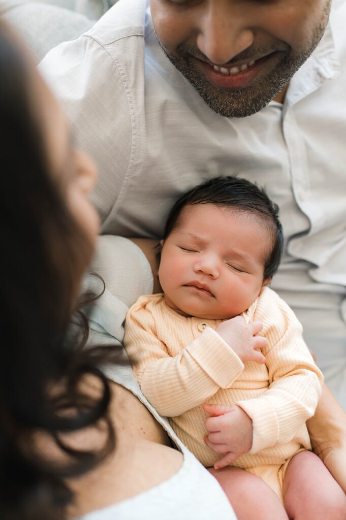 A Texas couple is pictured from above holding their newborn daughter as part of their in-home photo shoot with Towne Lake photographer, Mel B Photo.