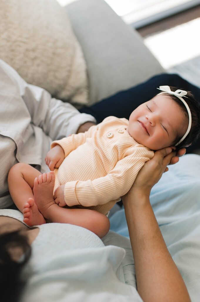 A newborn baby girl smiles in her sleep wearing a yellow romper during an in-home photo shoot with Bridgeland area newborn photographer, Mel B Photo.