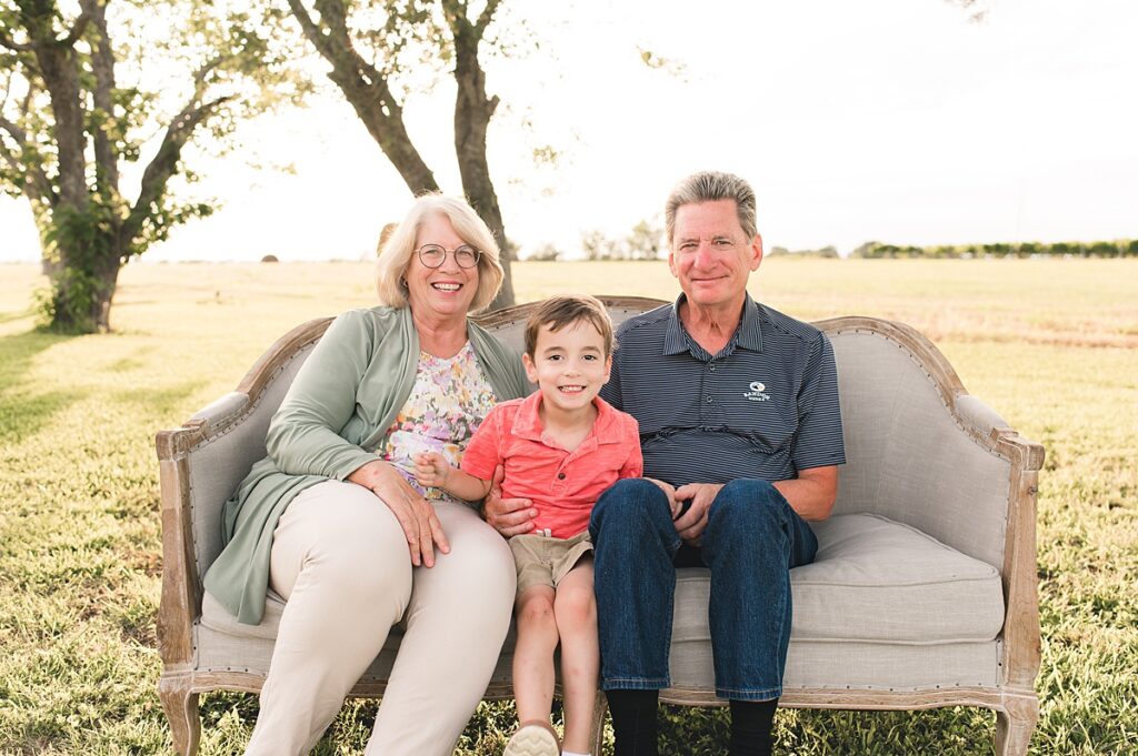 Texas grandparents are photographed on a tan sofa with their grandson during a golden hour outdoor family photo session with Cypress family photographer, Mel B photo.