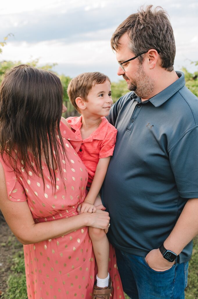 A brunette toddler wearing a polo smiles up at his father as his mother holds him on her hip during their Texas lifestyle photo session.