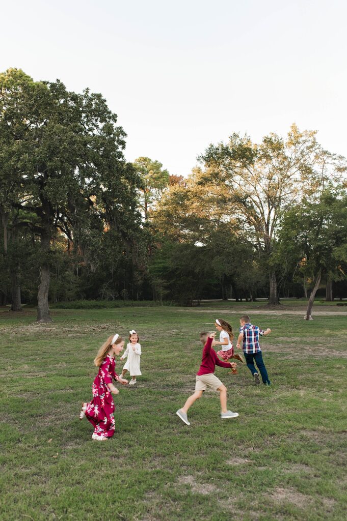 Five children chase each other in an open field, laughing & playing, during family pictures with Cypress area photographer, Mel B Photo.