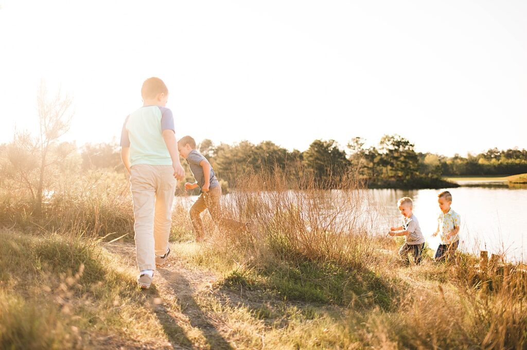 Four young brothers explore the the shore along a pond in Spring TX during their family photos at golden hour.