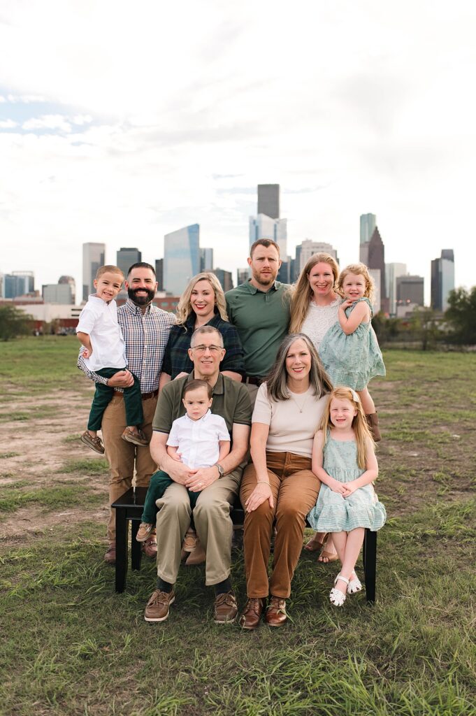 Multiple generations are photographed surrounding the matriarch and patriarch who are seated on a bench embracing two of their grandchildren with the Houston skyline and a strip of blue sky peeking through in the background.