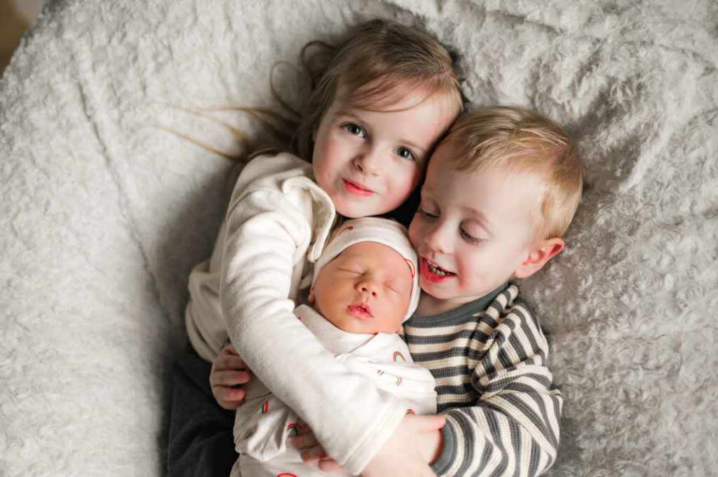 Two Houston area toddlers snuggle their newborn sibling in an example of how to plan wardrobe for family photos.