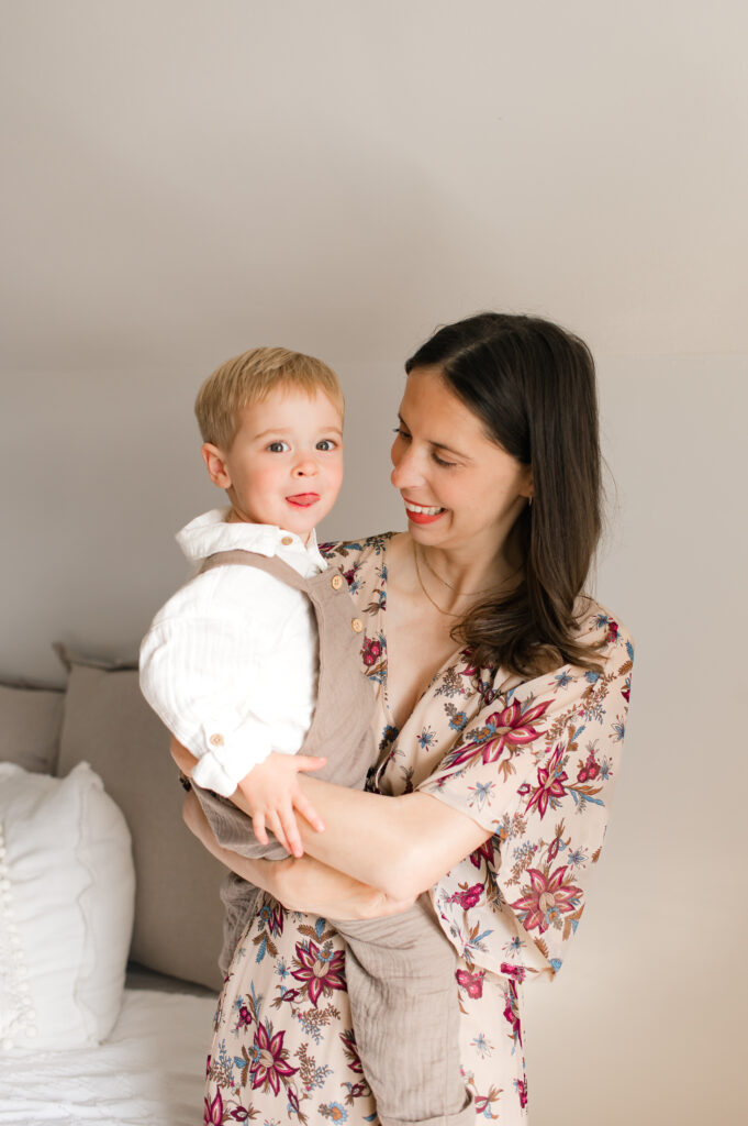 An example of how to integrate solids and prints into a family photo wardrobe is shown through a young brunette mother wearing a tan dress with deep shades of red florals holding her toddler son in a cotton shirt and brown, linen overalls.