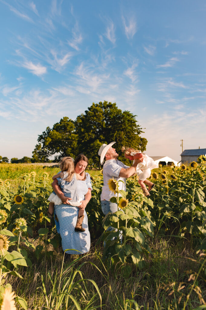 A family of four smiles in a Cypress TX area sunflower field wearing complementary shades of blue in various prints and fabrics.  This image is used as an example of how to plan your family photos wardrobe.