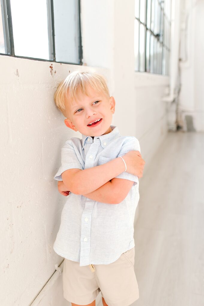 A blonde toddler boy crosses his arms and smiles for the  camera during Houston family photos with Woodlands family photographer, Mel B Photo 