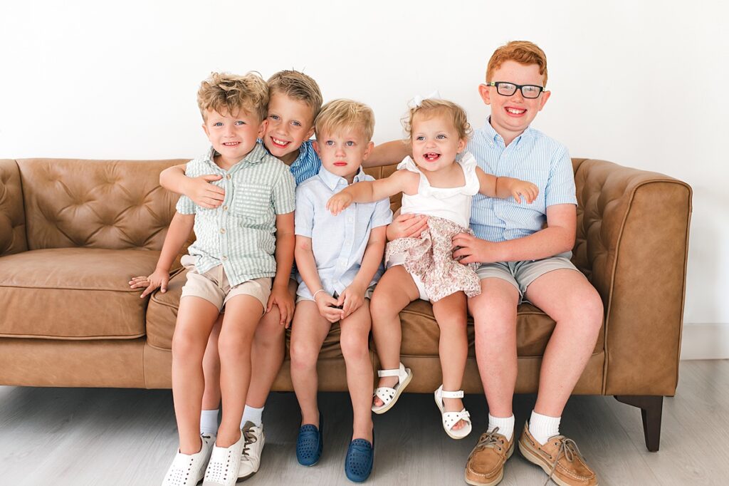 A group of cousins is photographed on a tan leather couch in a portrait studio Houston TX