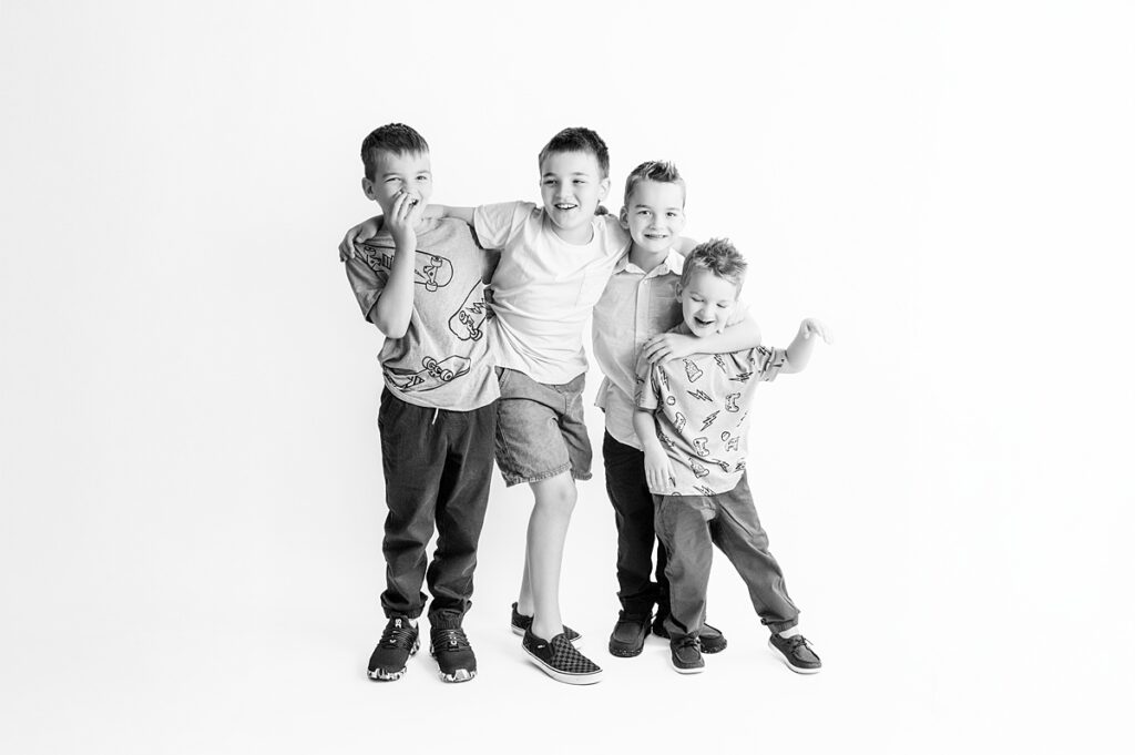 A black and white image of a studio Houston family session of four young boys linking arms 
