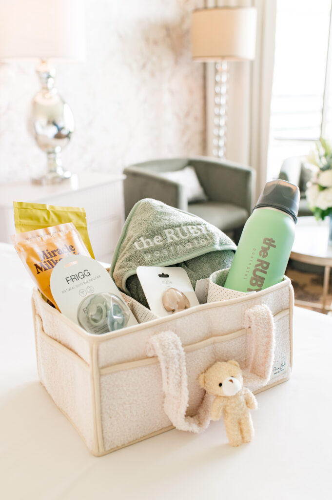 A gift basket for postpartum mothers is photographed in a luxury suite at The Ruby Postnatal featuring products from Miracle Milkookies, Ceres Chill, and Mushie