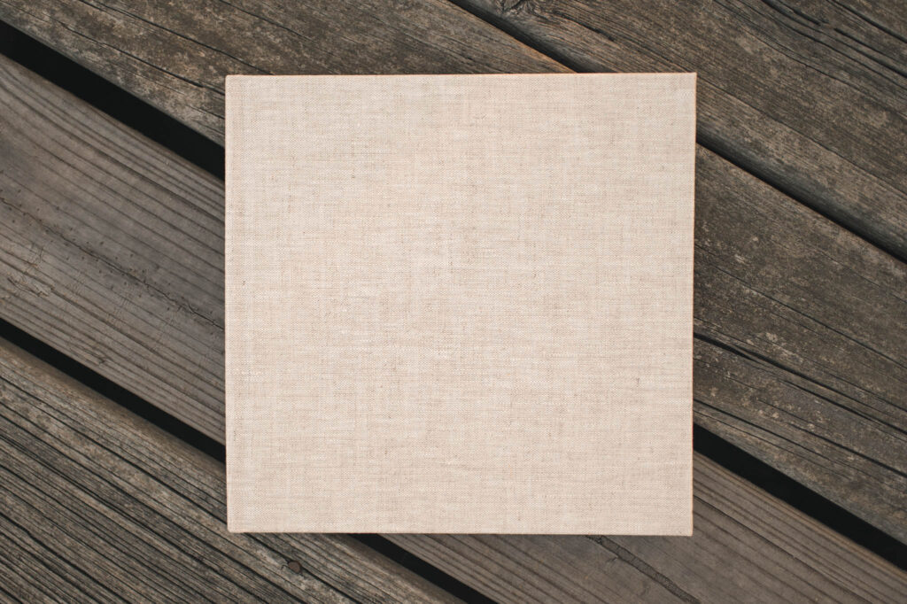 A linen photo album made by Houston family photographer, Mel B Photo, is photographed against a wooden floor