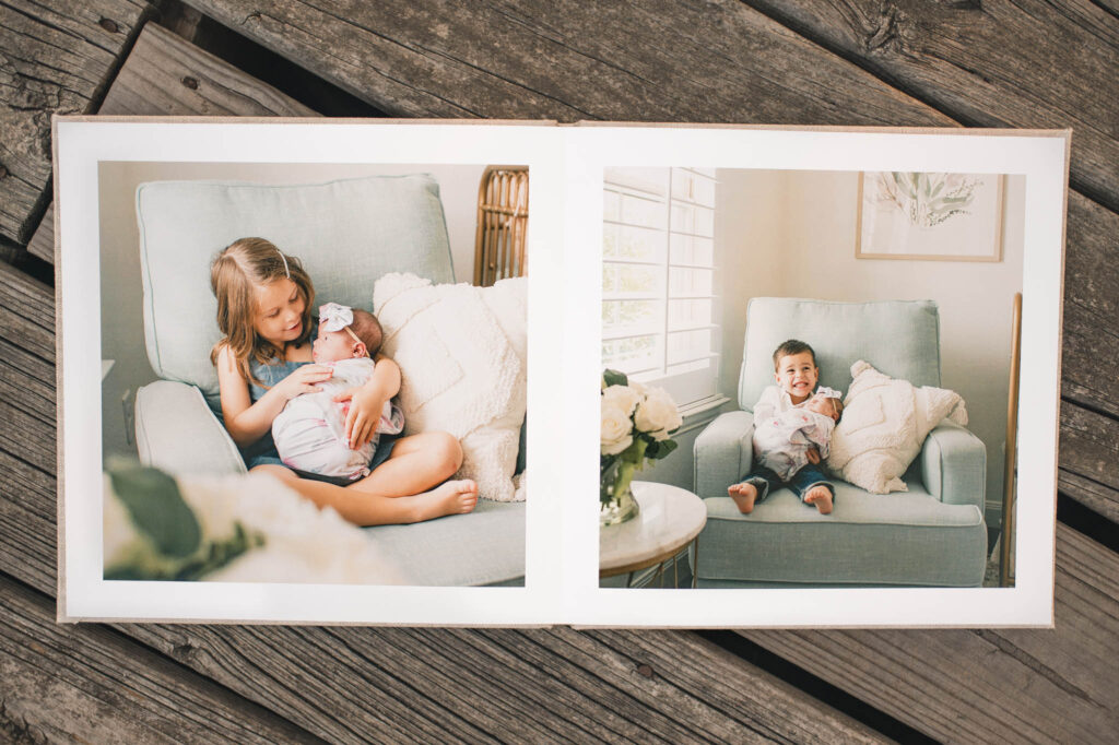 A photo book featuring Houston family pictures is shown open to a spread of two young children holding their newborn sister in a nursery rocker