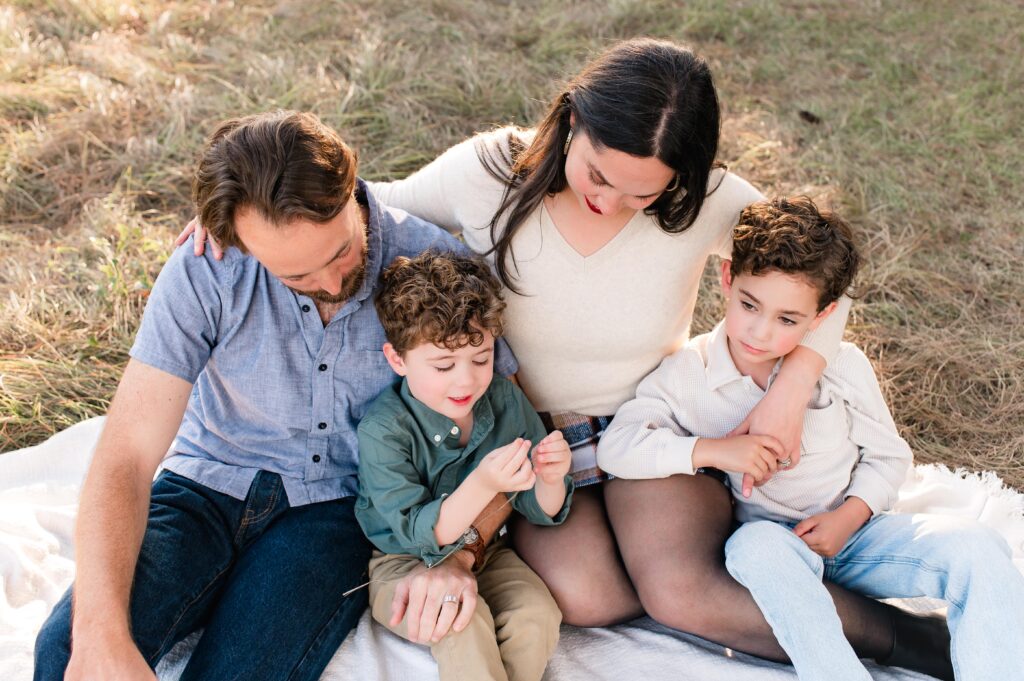 A family of four is seated on a blanket on the ground in a candid image taken during a Houston photo session with family photographer, Mel B Photo 