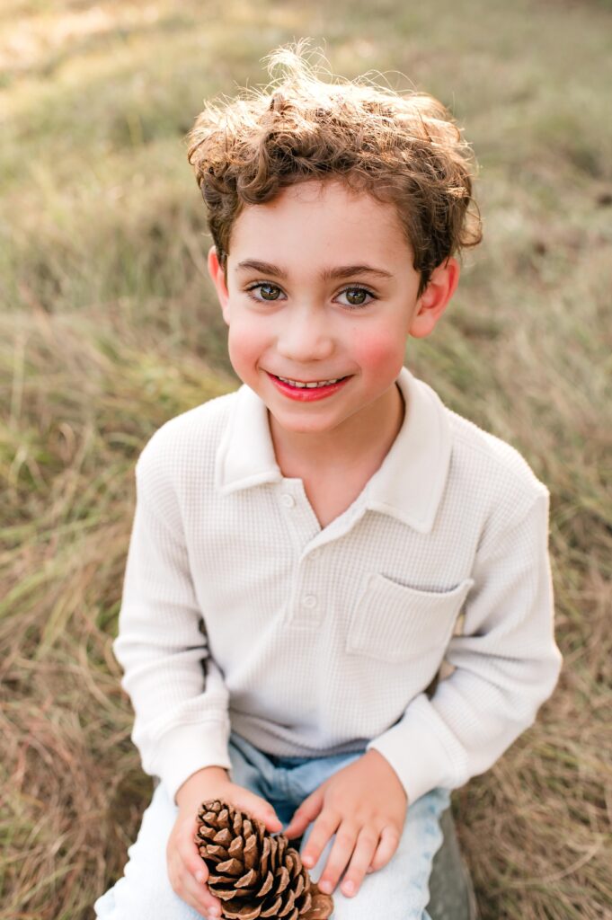 A young boy smiles as he holds a pine cone in a Houston photo taken at Cy Hope 