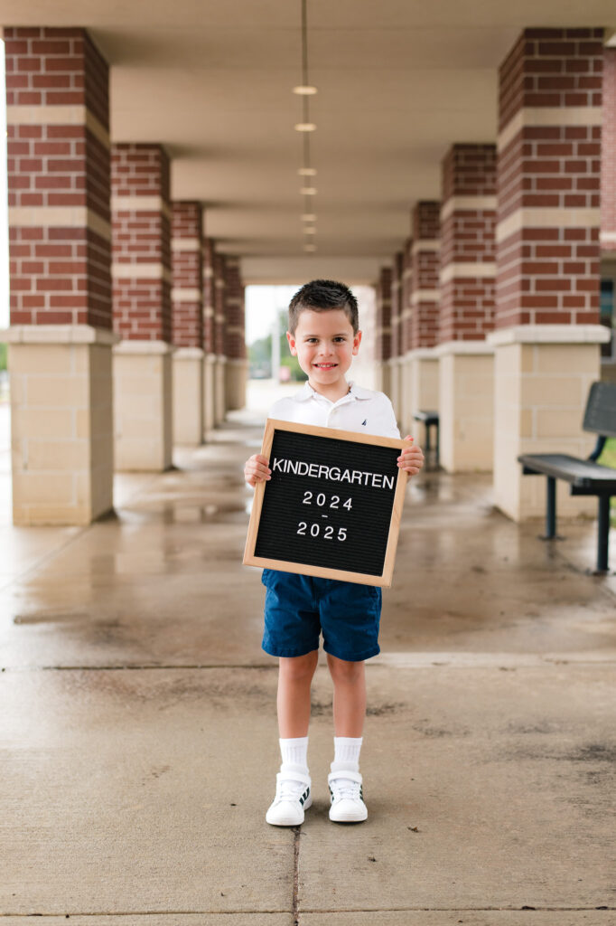 A young boy holds up a letter board that reads 'kindergarten 2024-2025' in a photo taken in a back-to-school mini session by Mel B Photo 