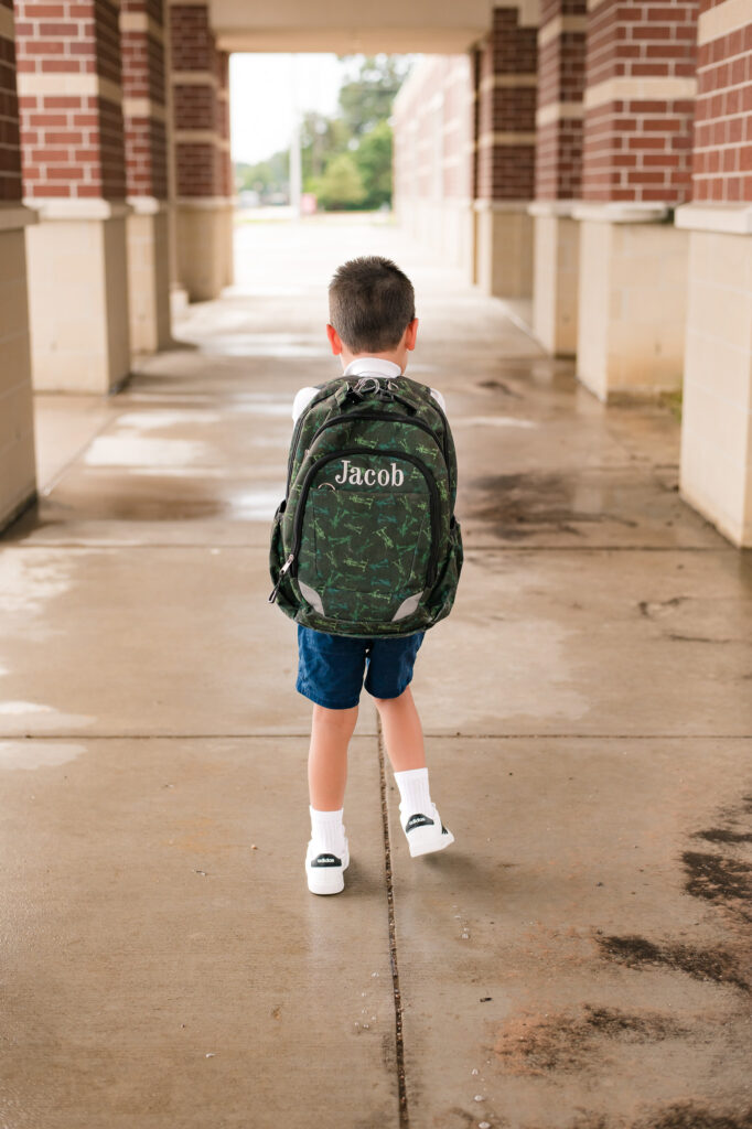 Back to school photography by Houston family photographer, Mel B Photo, showcases a young boy with a personalized backpack outside a Texas elementary school 