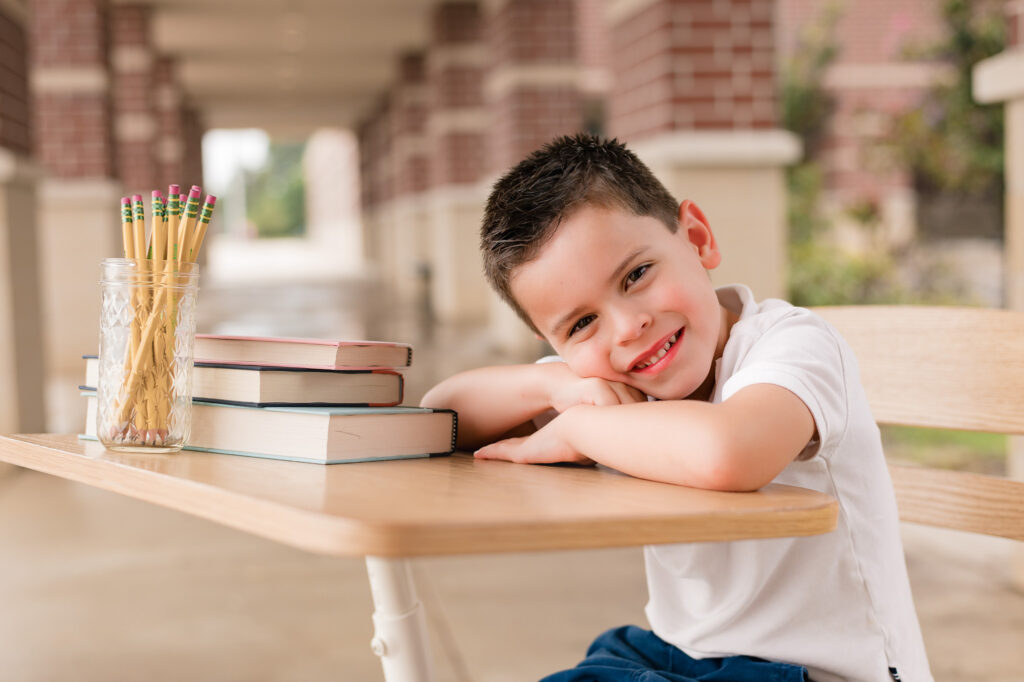 A young boy rests his head on a school desk next to a stack of books at a back to school session with child photographer in Houston, Mel B Photo