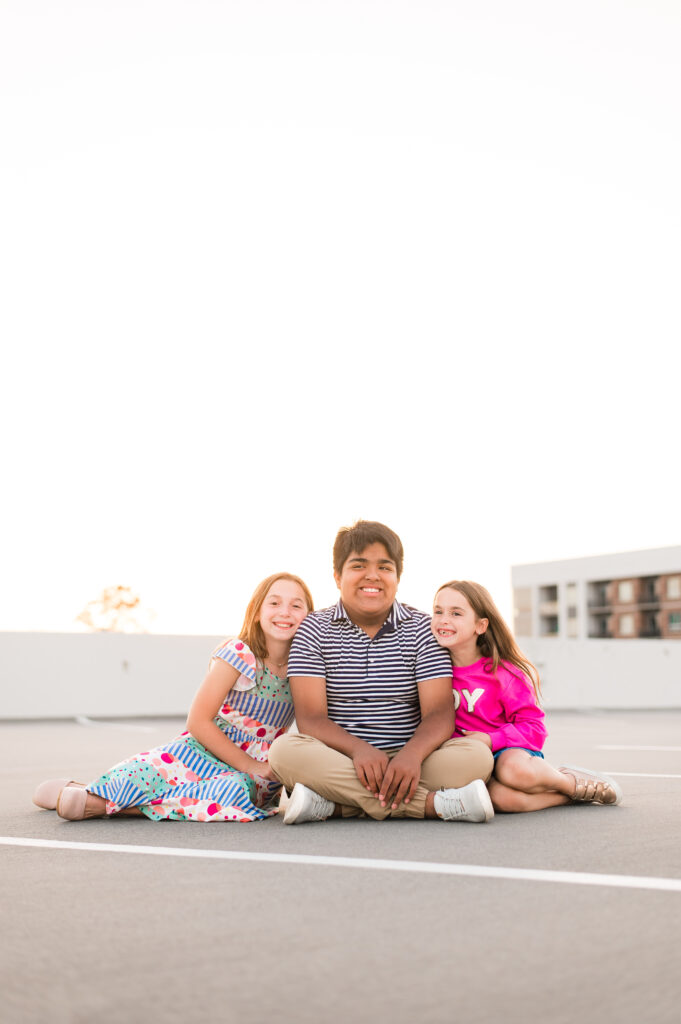 Three siblings smile seated on the ground during family pictures houston
