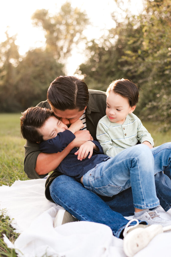 A father snuggles his two young sons on a blanket during family photography houston