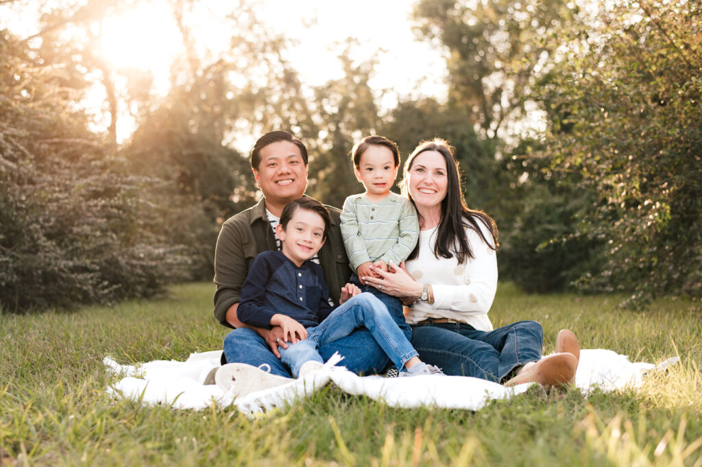 A family of four smiles on a blanket on the grass during family photos in houston in the fall
