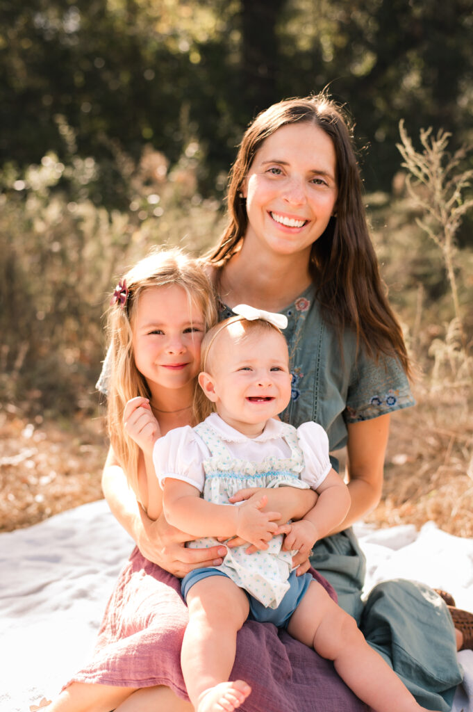 A young mother holds her two daughters on her lap during a family session with Houston family photographer, Mel B Photo 