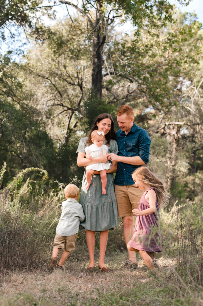A young couple with their three young children smile during outdoor family photos in houston in the fall