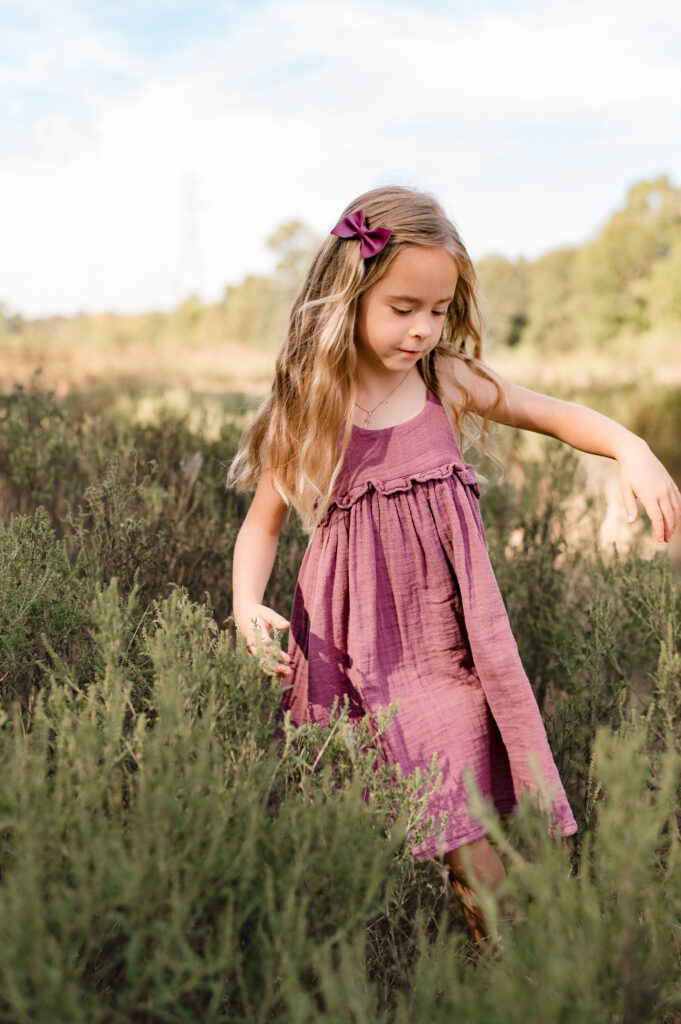 A young girl in a linen dress wades through knee high grass in a Texas field in Houston in the fall 