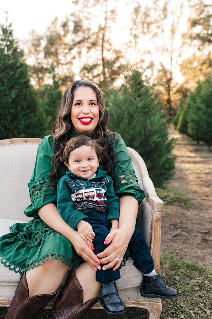 A mother holds her toddler son on her lap seated on a cream colored couch at a Houston TX Christmas tree farm