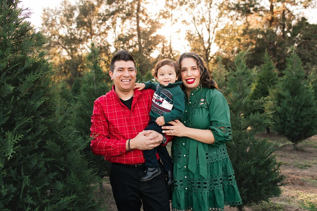 A Texas family of three lean in for a family photo at a Houston tree farm mini session 