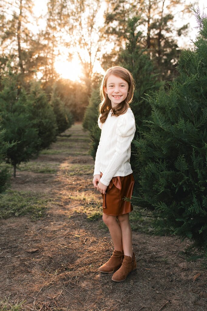 A young girl in a white sweater is photographed among the firs at a Christmas Tree Farm Houston family session