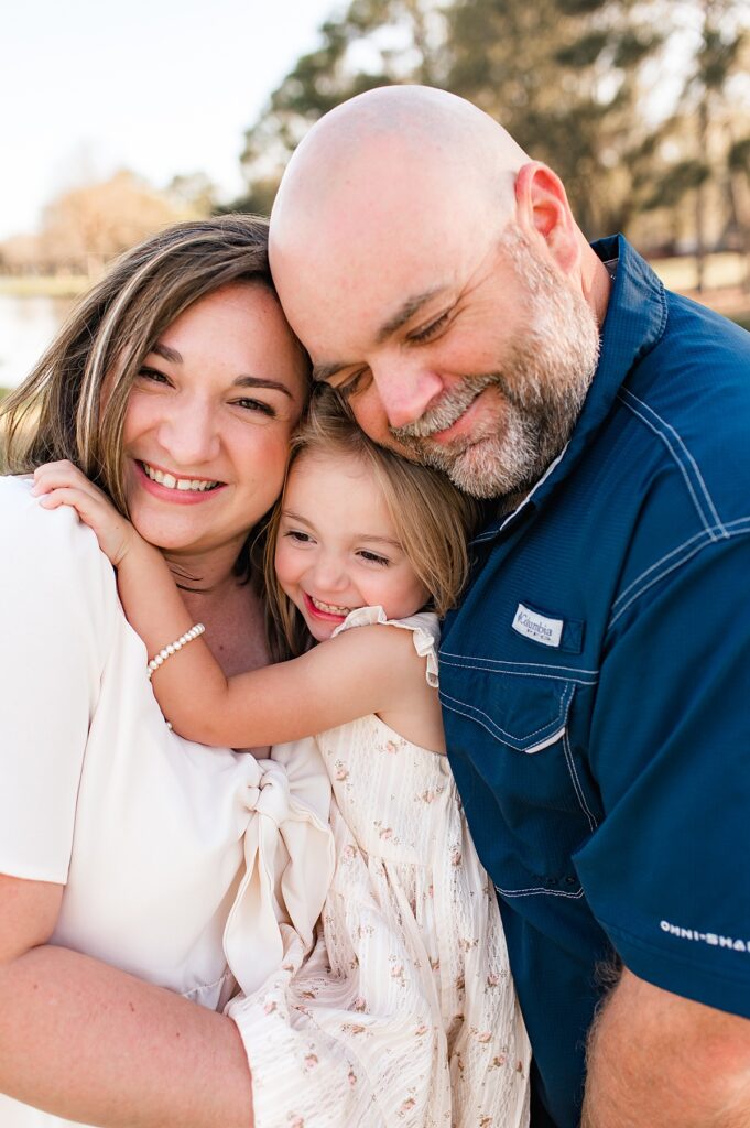 A mother & father snuggle their young daughter in Houston family pictures 