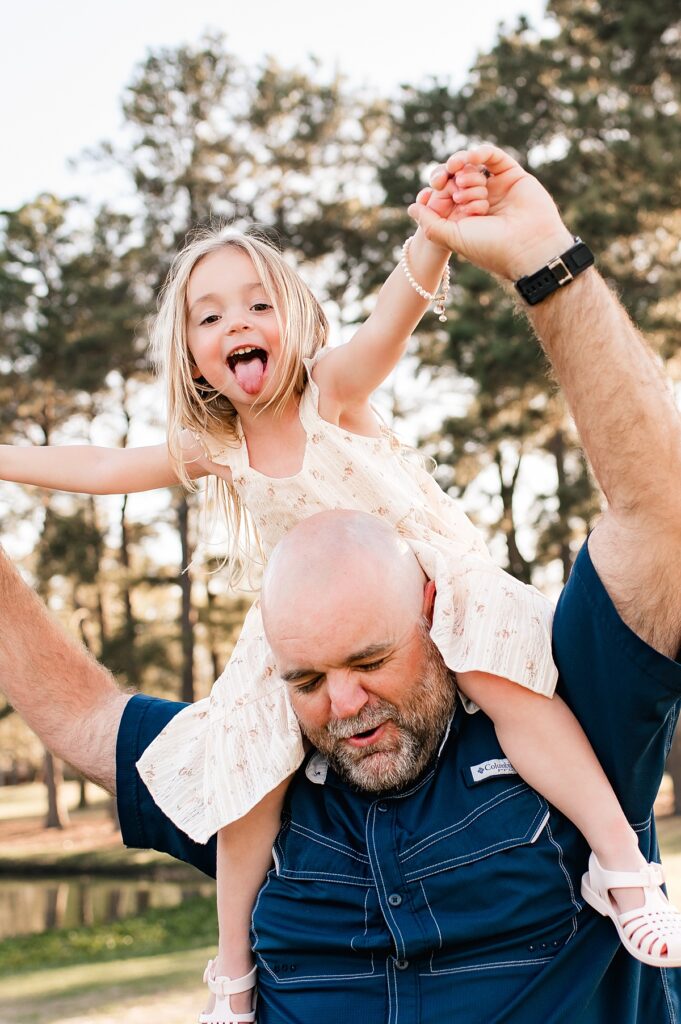 A young girl smiles while sitting on her father's shoulders during Houston Family Photos 