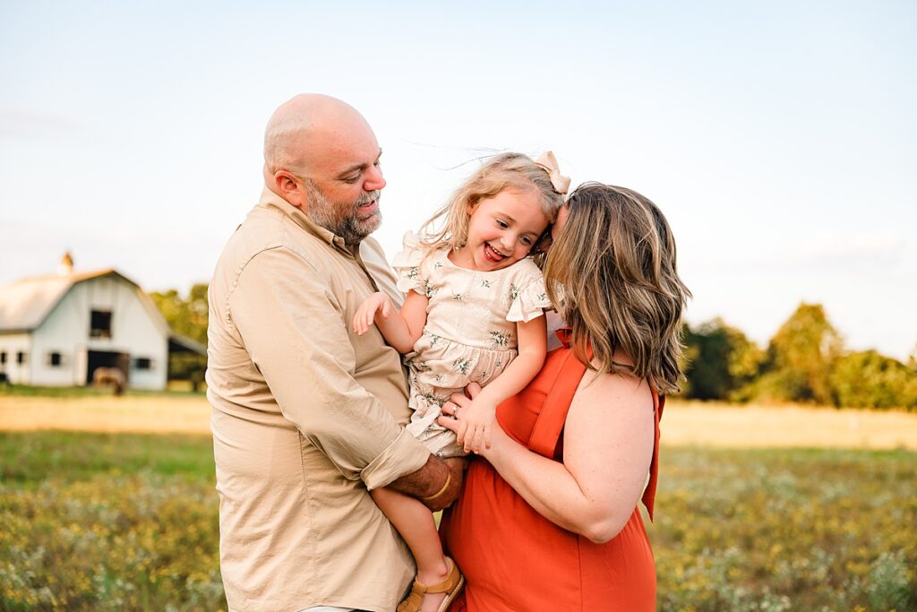 A mother and father snuggle their young daughter at Good Vibe Farm for  family photos Houston TX