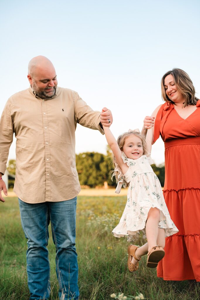 A mother & father swing their young daughter in a photo taken by Cypress photographer, Mel B Photo 