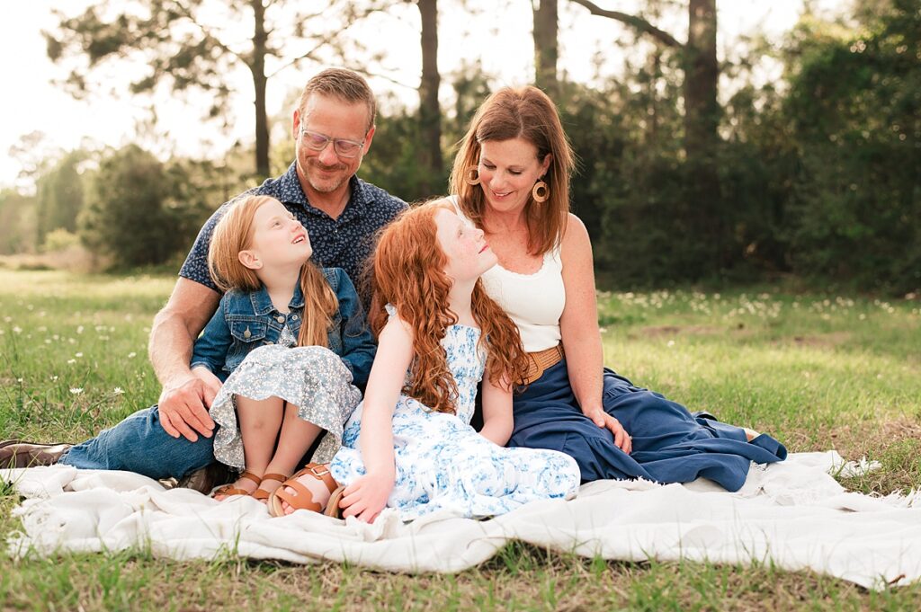 A family of four is seated on a blanket in a field during a photoshoot with a family photographer Cypress TX 