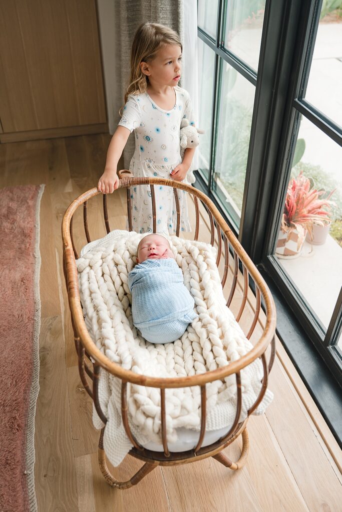  in-home newborn photography the woodlands tx depicts a newborn baby in a blue swaddle pictured with his older sister 