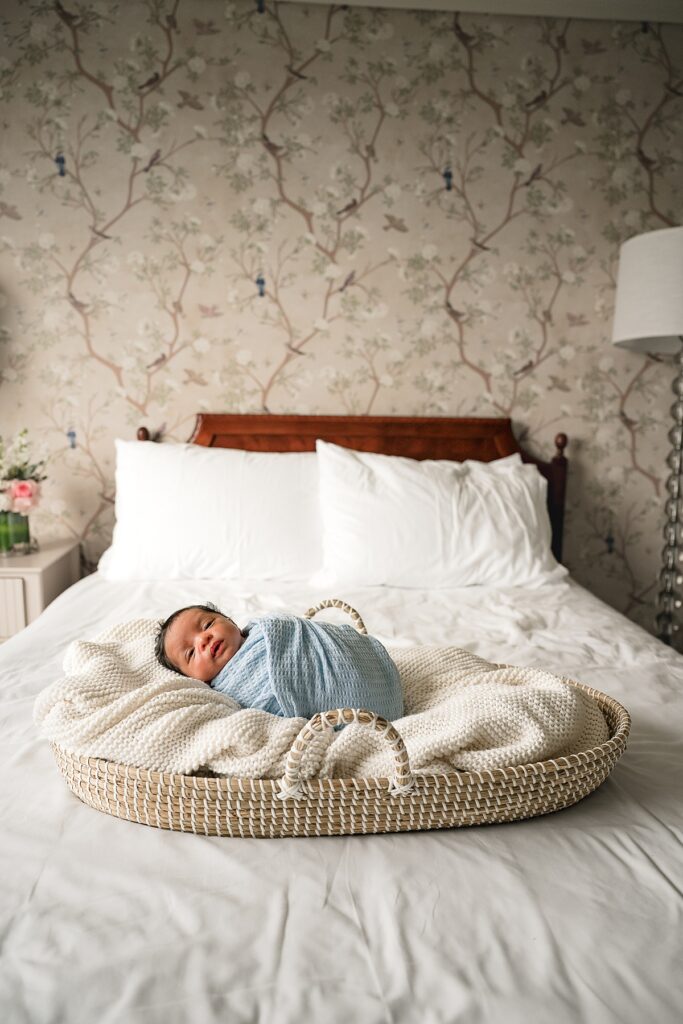 a photo taken during photography the woodlands tx depicts a newborn baby in a blue swaddle lying in a moses basket 