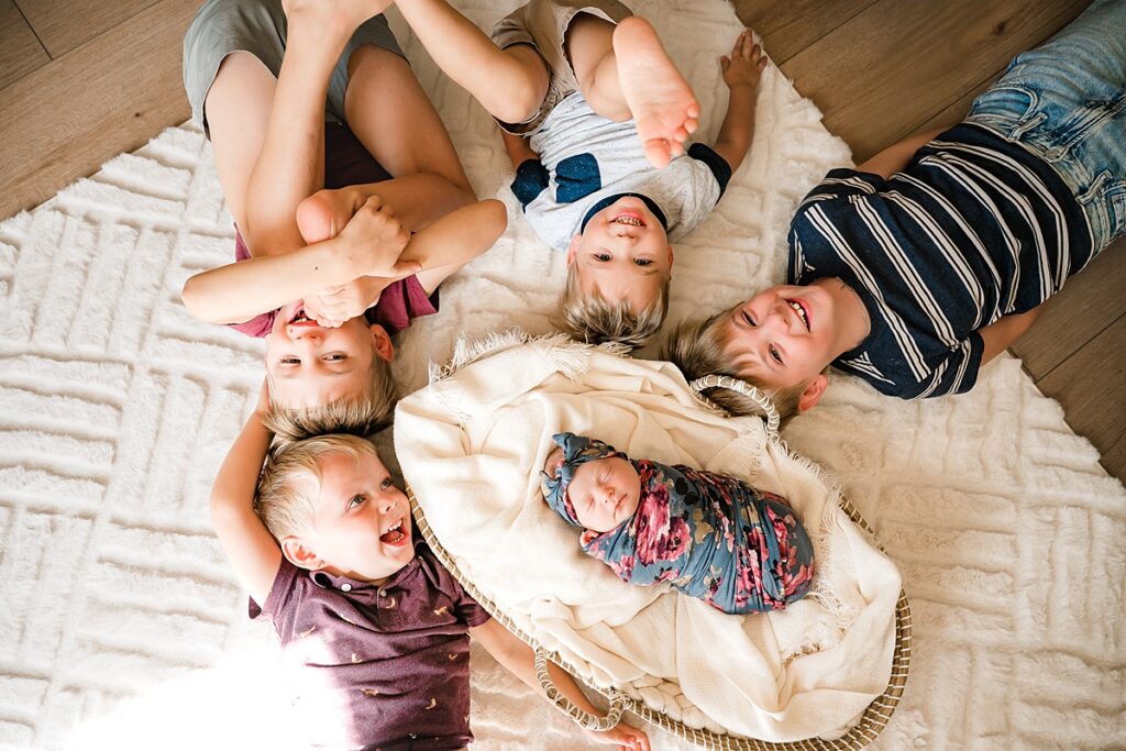 Four young boys pose with their infant sister in a photo taken during newborn photography the woodlands tx 