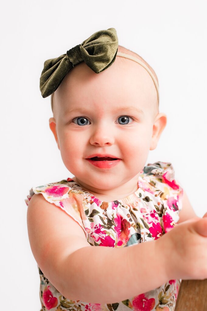 A toddler wearing a green bow and a floral shirt smiles in a Houston portrait